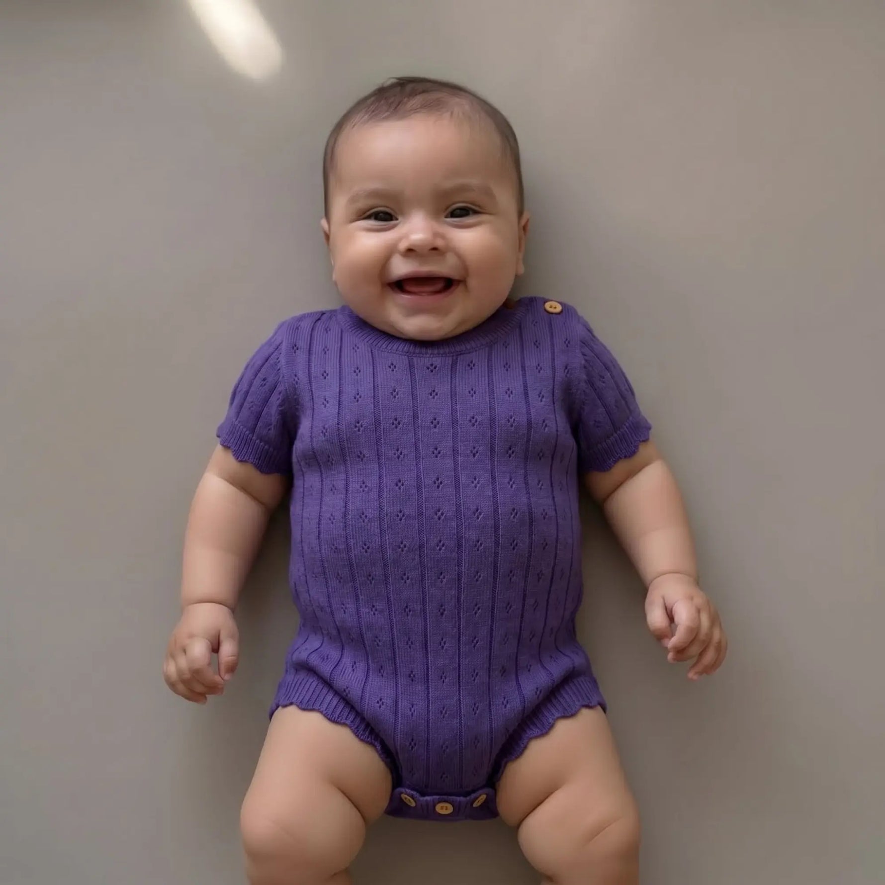 lachende baby in pointelle gebreide paarse romper 