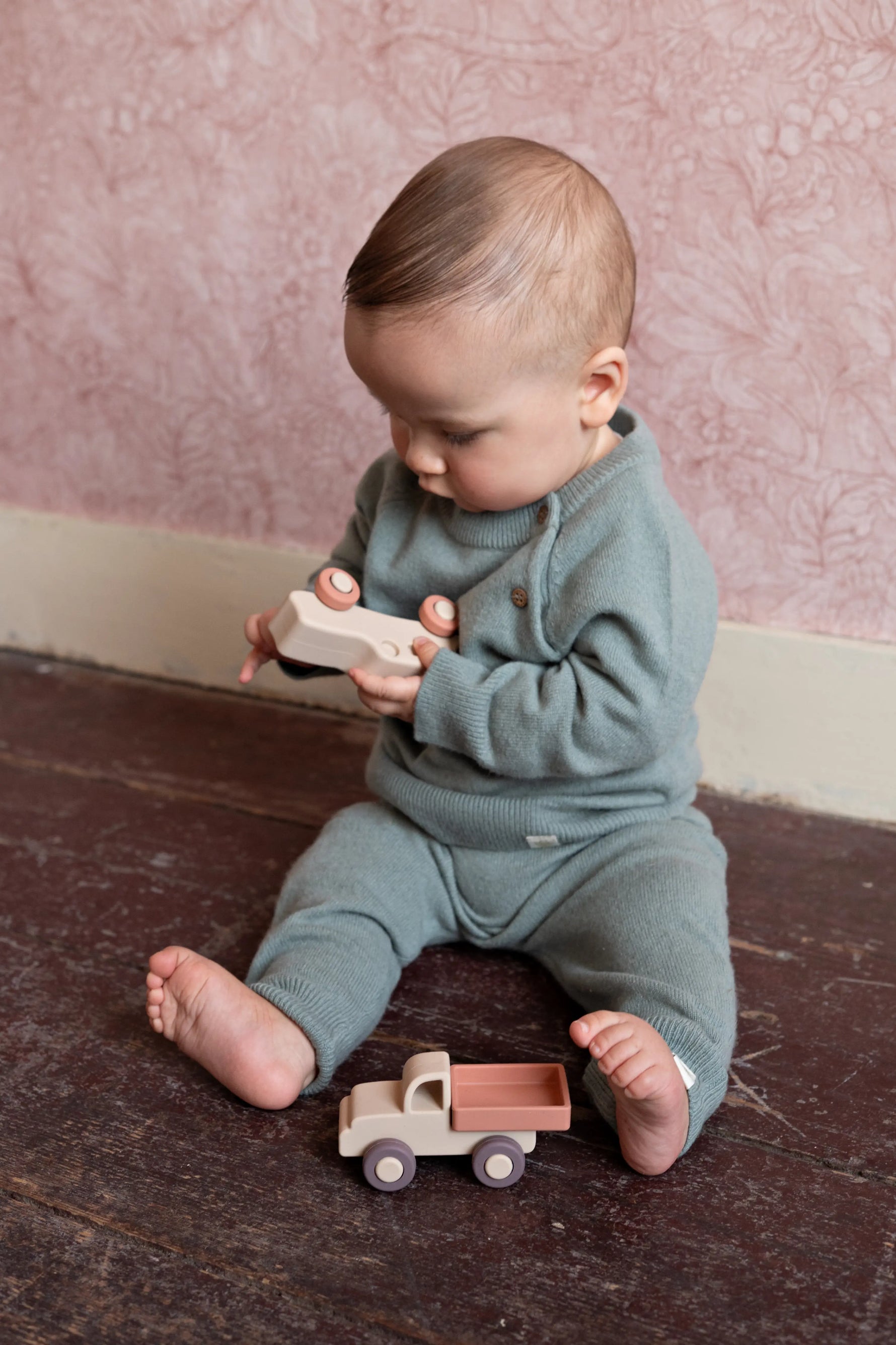 baby in sage groene wollen outfit van Moalie zittend op de grond en spelend met siliconen speelgoed auto's 