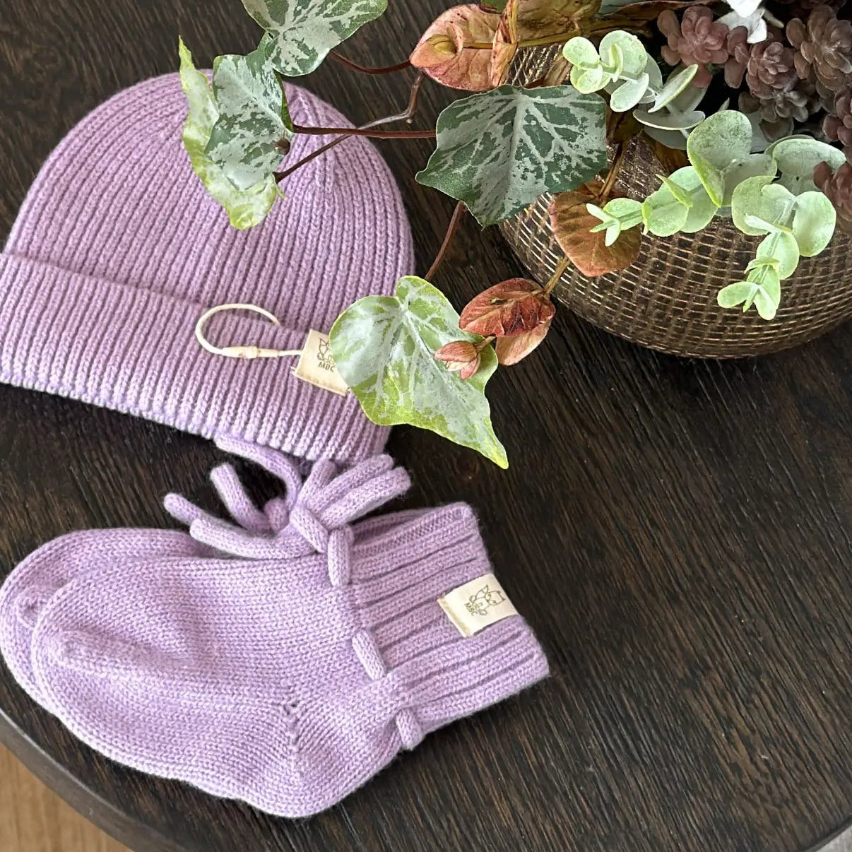 wollen baby set van muts en slofjes in lila kleur, gemaakt van 100% merinowol. Getoond op een bruinen houten bijzet tafeltje