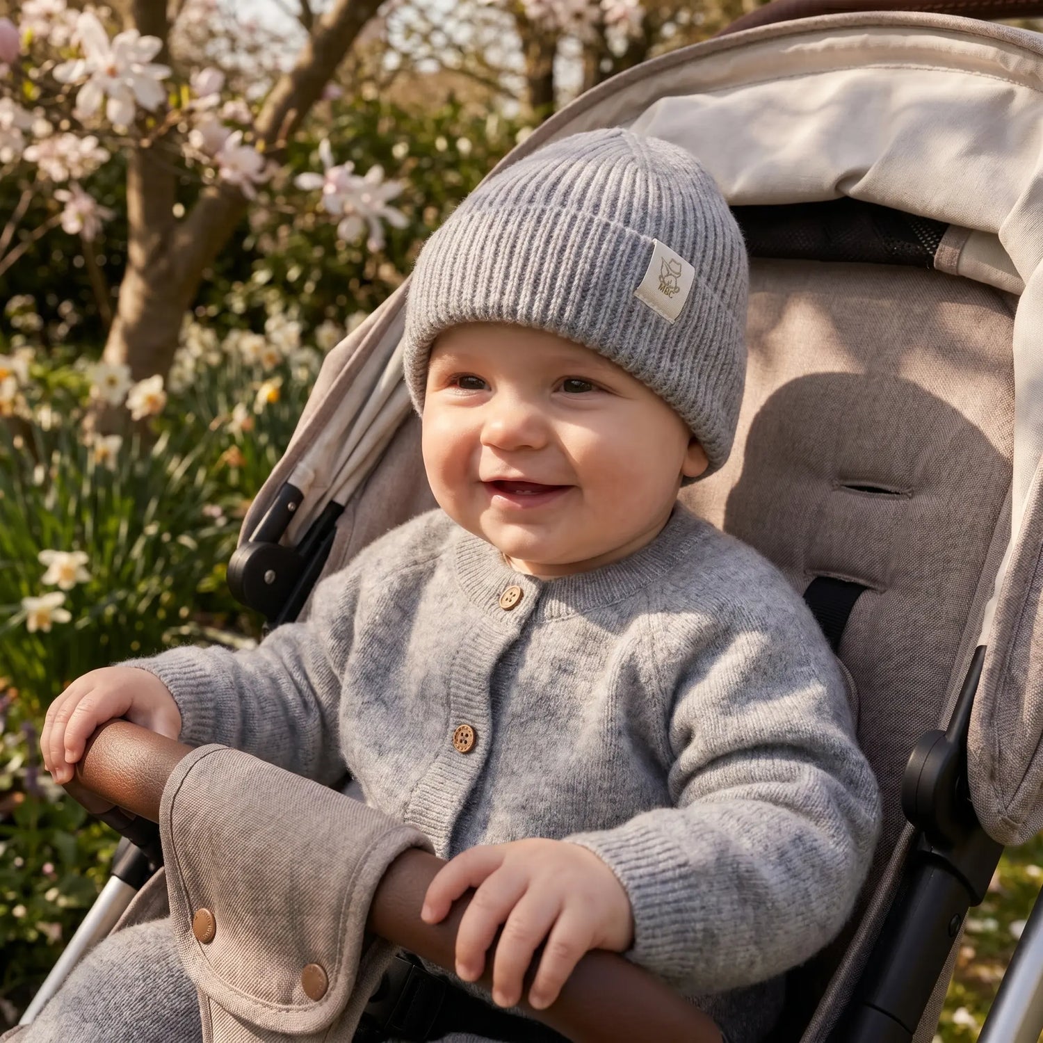 Baby zittend in buggy. De baby draagt een grijze wollen mutsje en vestje van Moalie van merinowol en cashmere 